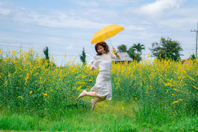 Portrait of woman with umbrella jumping against yellow flowering plants