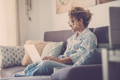 Woman using laptop while sitting on sofa at home