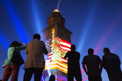 Rear view of people standing against illuminated building