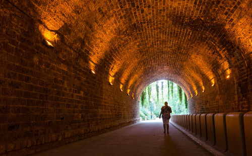 Rear view of woman walking in illuminated tunnel at park