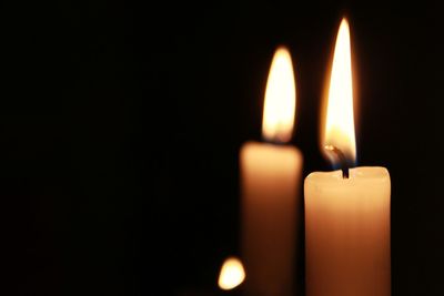 Close-up of burning candles against black background