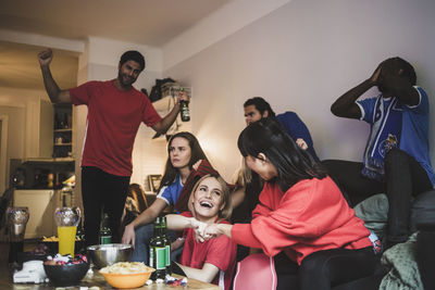 Cheerful red team celebrating while blue team sitting in disappointment at home