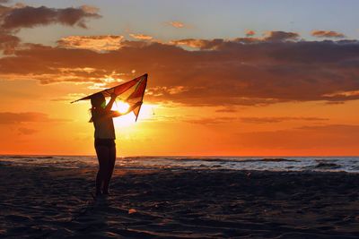 Silhouette person standing on beach against sky during sunset