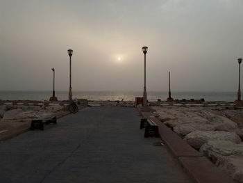Street by sea against sky during sunset