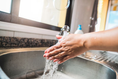 Cropped image of person washing hand in sink