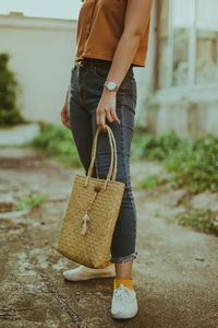 Low section of woman holding wicker bag while standing outdoors