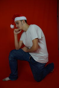 Thoughtful man wearing santa hat looking away against red background