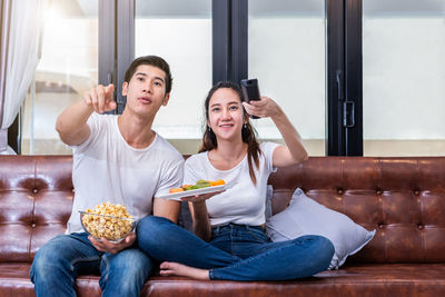 Friends watching television while having food on sofa at home