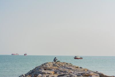 Man fishing while crouching on groyne against sky