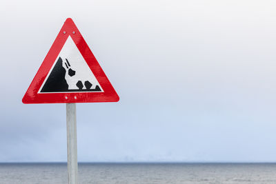 Close-up of road sign by sea against clear sky