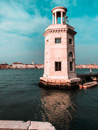 Lighthouse by sea against buildings in city