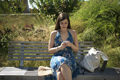 Woman using smart phone while sitting on bench at park