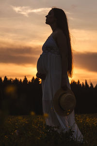 Side view of woman standing on field against sky during sunset