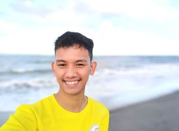 Portrait of young man standing at beach against sky