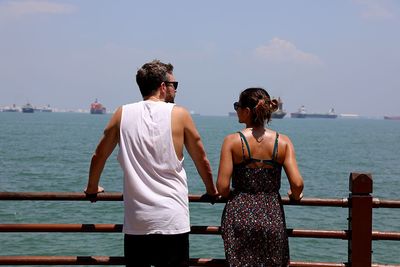 Rear view of man and woman standing by railing against sea