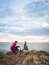 Man sitting on rock by sea against sky