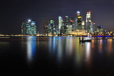 Illuminated buildings by river against sky at night