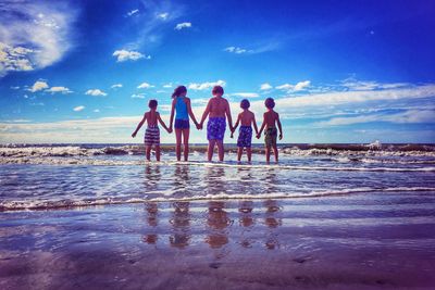 Rear view of people enjoying at beach against sky