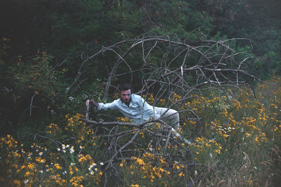 Young man sitting amidst branches on field