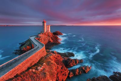 Lighthouse by sea against sky during sunset