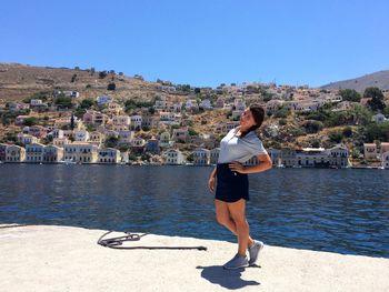 Woman standing on retaining wall by river against clear blue sky