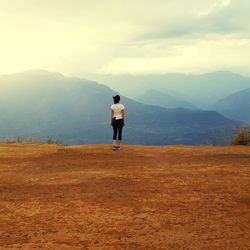 Rear view of man standing on mountain against sky