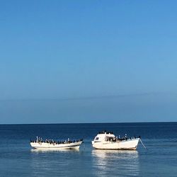 Boats sailing in sea against clear sky