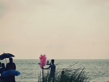 Men standing at beach against clear sky