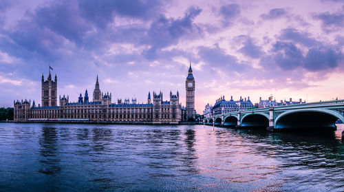 Westminster bridge over thames river against big ben against cloudy sky