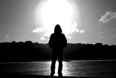 Silhouette man standing by river against sky