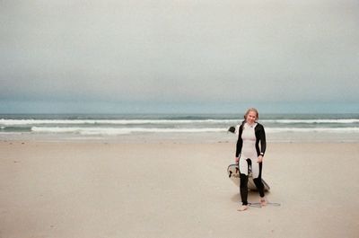 Full length of young woman standing on beach against sky