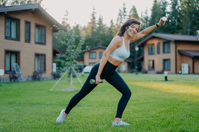 Portrait of smiling woman lifting dumbbells on grassy land