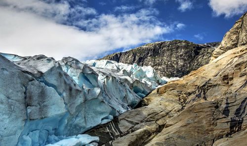 Low angle view of glacier and rocky mountains against sky