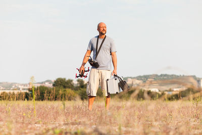 Mid adult man with drone standing on grassy field against clear sky