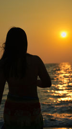 Rear view of woman standing at beach against sky during sunset