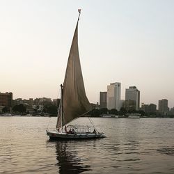 Sailboat sailing on sea against buildings in city