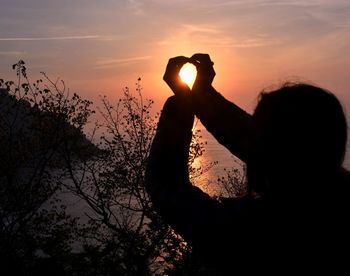 Close-up of silhouette hand against sunset sky