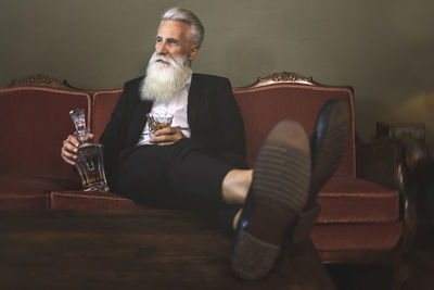 Full length of mature man holding drink sitting on sofa