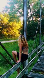 Young woman sitting on railing against trees