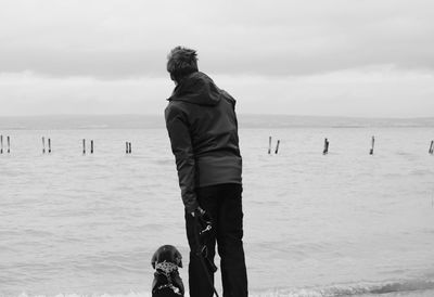 Rear view of man standing with dog at beach