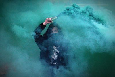 Young woman holding distress flare outdoors