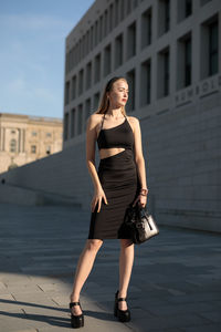 Full length of young woman standing on footpath in city