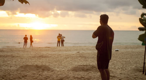 Rear view of man on beach against sky during sunset