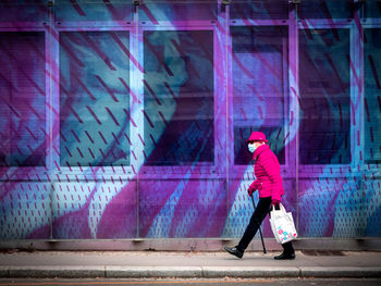 Full length of man holding umbrella standing against graffiti wall