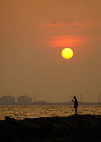 Silhouette person on rocky beach against sky during sunset