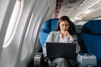 Businesswoman with hand on chin using laptop in plane