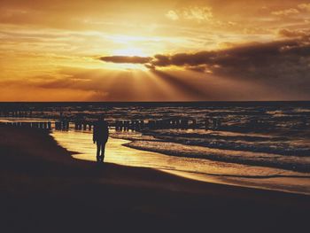 Silhouette person standing on beach against sky during sunset