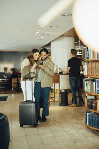 Couple with luggage using smart phone while standing in restaurant