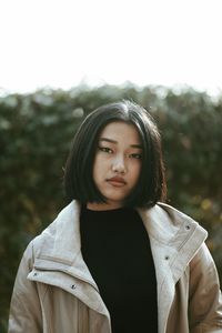 Portrait of young woman standing against trees