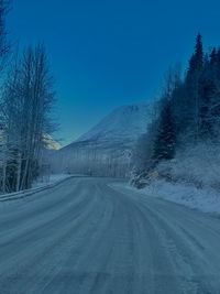 Road amidst snow covered trees against clear sky